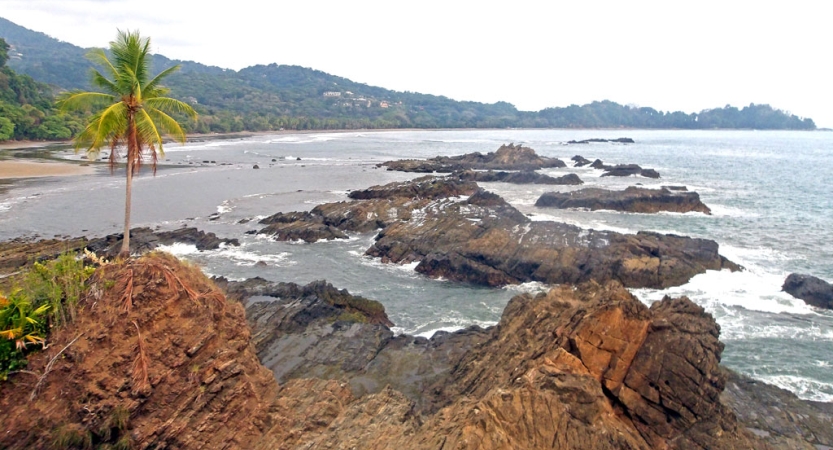 Green hills hug the shoreline and rocks reach out into the ocean.